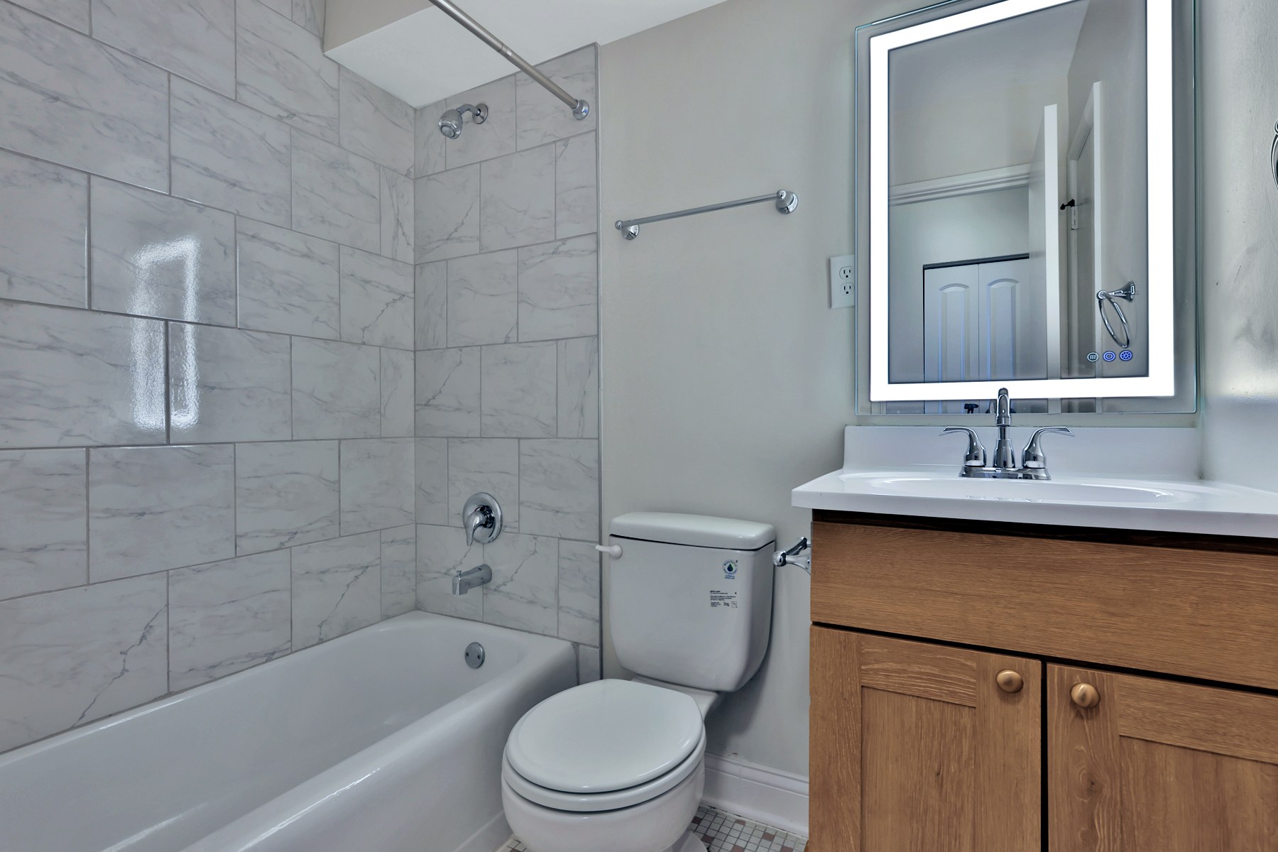 A renovated bathroom with a white subway-tile tub surround and wood vanity