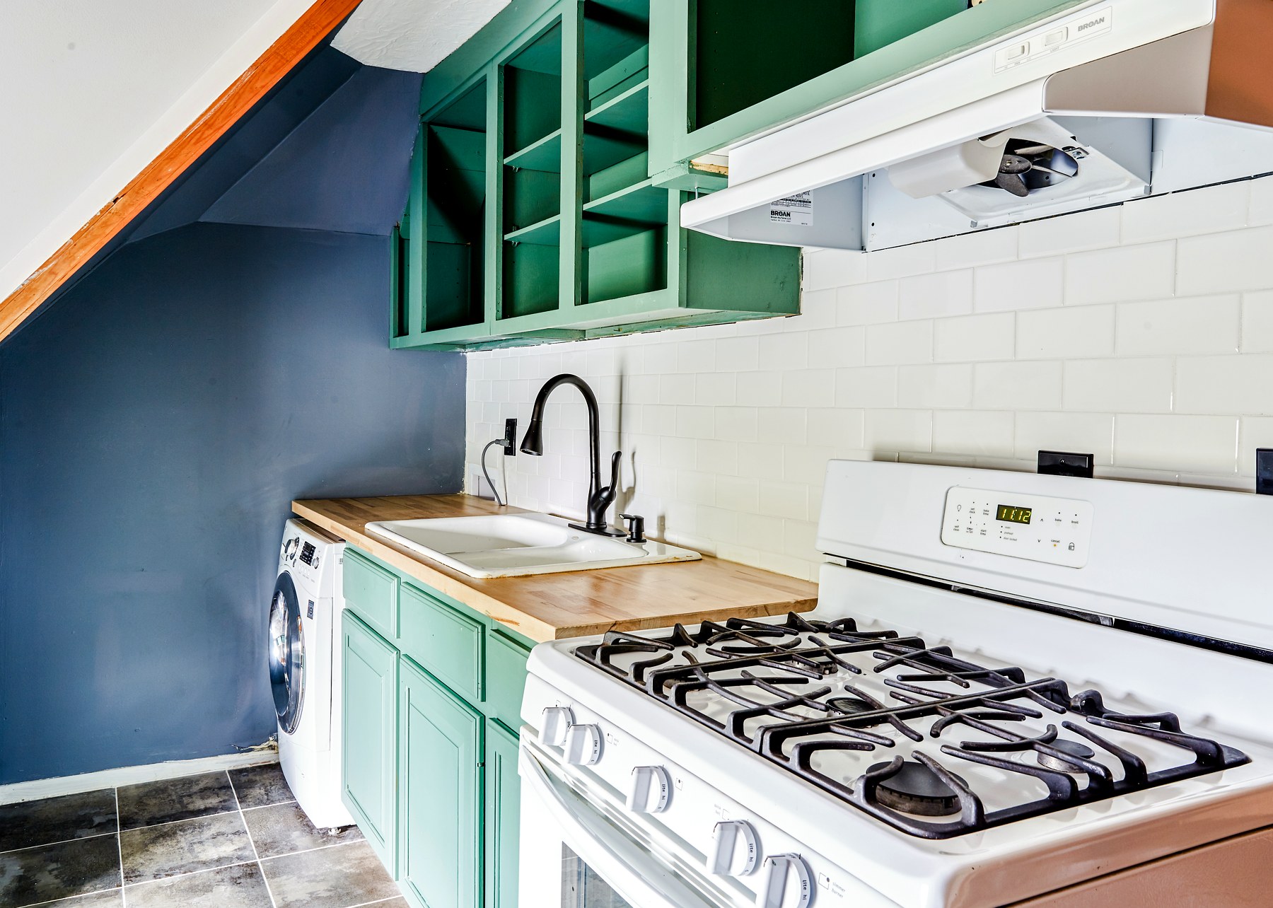 A renovated kitchen with mint-green cabinets, a gas range, and butcher-block counters